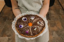Do bolo apetitoso acima mencionado festivamente decorado com flores brilhantes em mãos de mulher — Fotografia de Stock
