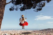 Menina se divertindo com saia vermelha e chapéu balançando enquanto contempla a cidade no fundo — Fotografia de Stock