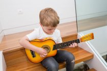 Jovem loira menino concentrando-se enquanto tocava guitarra — Fotografia de Stock