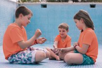 Bambini in vivaci t-shirt arancioni seduti sul fondo della piscina vuota e giocare a sasso-carta-forbici — Foto stock
