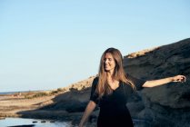 Joven mujer sonriente mirando hacia la costa rocosa — Stock Photo