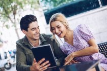 Cheerful young attractive couple using digital tablet outdoors in town — Stock Photo