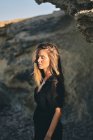 Jovem de cabelos longos elegante mulher pensativa em pé na luz do sol com rocha no fundo — Fotografia de Stock