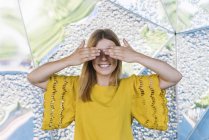 Junge verspielte Frau, die Augen mit Händen auf Metallhintergrund bedeckt — Stockfoto