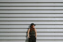 Frau mit schwarzem Hut lehnt an grau gestreifter Wand — Stockfoto