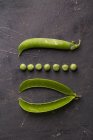 Peeled fresh peas and pea pods on dark background — Stock Photo