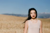 Красивая азиатская женщина смотрит в камеру, стоя на размытом фоне луга в ветреный день на природе — стоковое фото