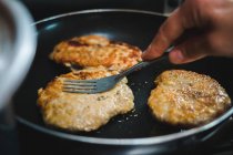 Primi piani di coltura mano di persona anonima cottura deliziose tagliatelle di carne friggere su olio su padella calda in cucina — Foto stock