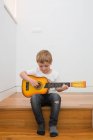 Молодой блондин концентрируется во время игры на гитаре — стоковое фото