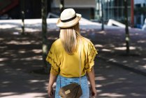 Вид на молодую стильную блондинку в соломенной шляпе, гуляющую по городу в летний день — стоковое фото
