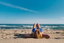Расслабленная женщина наслаждается хорошей погодой, лежа на песчаном пляже в яркий день — стоковое фото