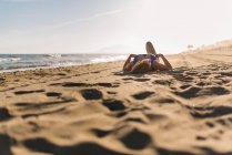 Mujer relajada disfrutando del buen tiempo tumbado en la playa de arena en un día brillante - foto de stock