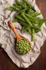Fresh peas in a wooden scoop on cloth on wooden table — Stock Photo