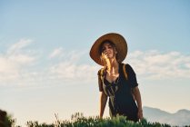 Turista feminina usando chapéu de palha e mochila andando na natureza e olhando para a câmera — Fotografia de Stock