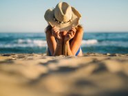 Gebräunte Frau bedeckt Gesicht mit Hut und sonnt sich an sonnigem Tag am Sandstrand — Stockfoto