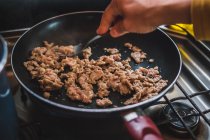Неизвестные отжимают мясной фарш вилкой на сковороде во время приготовления пищи на кухне — стоковое фото