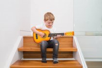 Jeune garçon blond se concentrant tout en jouant de la guitare — Photo de stock