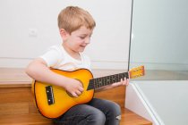 Jeune garçon blond se concentrant tout en jouant de la guitare — Photo de stock