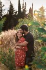 Homem pensativo abraçando sorridente esposa grávida no fundo do pitoresco parque verde no dia ensolarado — Fotografia de Stock