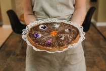 Зверху смачний апетитний торт святково прикрашений яскравими квітами в руках жінки — стокове фото