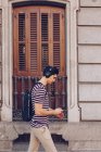 Jeune homme attrayant en vêtements décontractés écoutant de la musique pendant la marche dans la rue en plein jour — Photo de stock