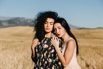 Frau mit geschlossenen Augen stützt sich auf die Schulter ihres Freundes, während sie in einem Feld mit trockenem Gras in der Nähe von Hügeln steht — Stockfoto