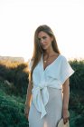 Junge elegante Frau in weißen Kleidern blickt in die Kamera in der Natur — Stockfoto