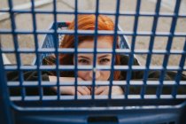 Woman looking through trolley grate in shopping cart — Stock Photo
