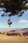 Menina se divertindo com saia vermelha e chapéu balançando enquanto contempla a cidade no fundo — Fotografia de Stock