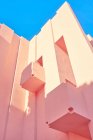 Edificio rosa de forma geométrica compleja bajo el cielo azul - foto de stock