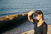 Giovane donna attraente che copre il viso dal sole sulla spiaggia — Foto stock