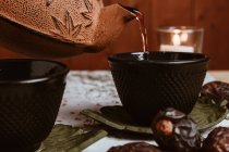 Sirve té sabroso fragante en taza de tetera de arcilla y dátiles dulces en bandeja blanca decorada con hojas de té sobre fondo de madera - foto de stock