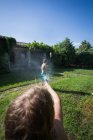 Crianças em trajes de banho correndo e salpicando água da mangueira de jardim um para o outro, vista em primeira pessoa — Fotografia de Stock