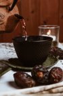 Servire profumato tè gustoso in tazza di teiera di argilla e datteri dolci su vassoio bianco decorato con foglie di tè su sfondo di legno — Foto stock