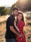 Uomo che abbraccia sorridente moglie incinta sullo sfondo della natura nella giornata di sole — Foto stock