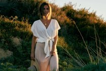 Giovane donna attraente in vestiti bianchi guardando la fotocamera in natura al tramonto — Foto stock