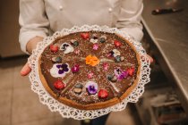 Do bolo apetitoso acima mencionado festivamente decorado com flores brilhantes em mãos de mulher — Fotografia de Stock