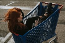 Donna sorridente utilizzando smartphone nel carrello della spesa nel parcheggio — Foto stock