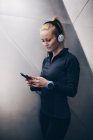Молода блондинка біла жінка зі спортивним одягом слухає музику з навушниками, підключеними до її смартфона — стокове фото
