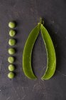 Peeled fresh peas in a row and pea pod on dark background — Stock Photo