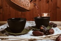 Serving fragrant tasty tea in cup clay teapot and sweet dates on white tray decorated with tea leaves on wooden background — Stock Photo