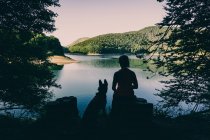 Mujer con perro descansando sobre hermoso lago - foto de stock