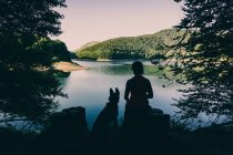 Mulher com cão descansando contra belo lago — Fotografia de Stock