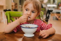 Nourriture parfumée appétissante dans un bol blanc et adorable fille mangeant avec les mains à la table — Photo de stock