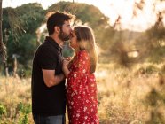 Чоловік обіймає усміхнену вагітну дружину на фоні мальовничого зеленого парку в сонячний день — стокове фото