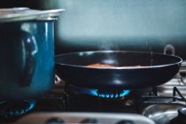 Крупним планом великий металевий кухоль і сковорідку поміщають у вогонь газової плити на кухні — стокове фото
