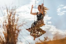 Happy girl with dress enjoying on a swing at sunset — Stock Photo