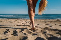 Vista posterior de las piernas recortadas femeninas con sombrero de paja en la costa a la luz del sol brillante - foto de stock