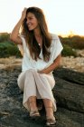 Elegante giovane donna seduta e sorridente sulla roccia nella natura al tramonto — Foto stock