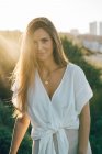 Giovane donna sorridente in abiti bianchi in piedi alla luce del sole — Foto stock